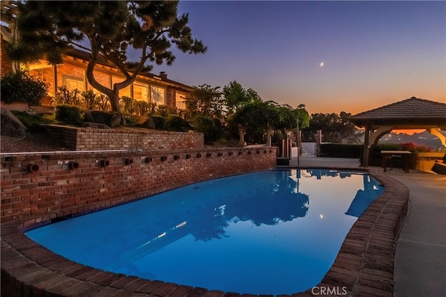 pool at dusk with a gazebo and a patio