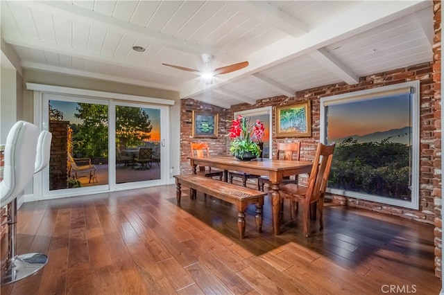 dining room featuring beamed ceiling, hardwood / wood-style flooring, brick wall, and ceiling fan