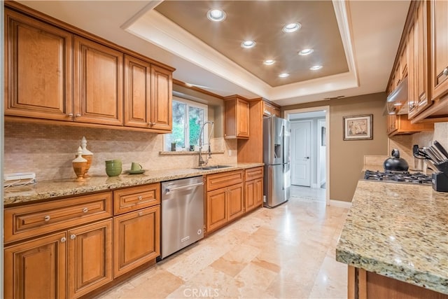 kitchen with stainless steel appliances, light stone countertops, backsplash, and a tray ceiling