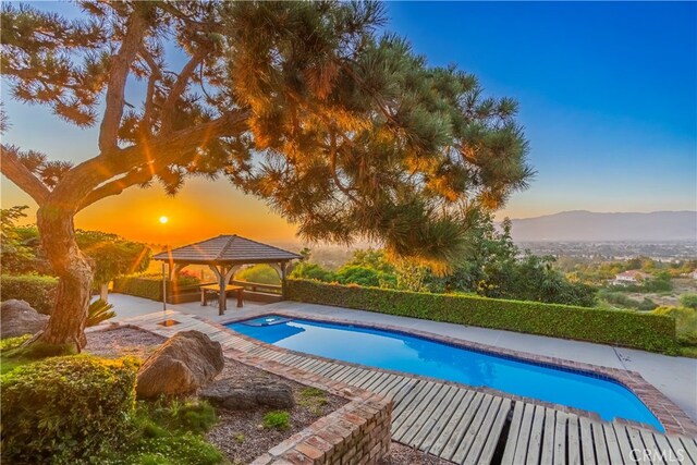 pool at dusk featuring a mountain view, a gazebo, and a patio area