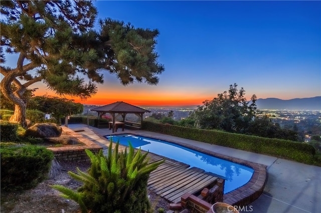 pool at dusk with a mountain view, a gazebo, and a patio area