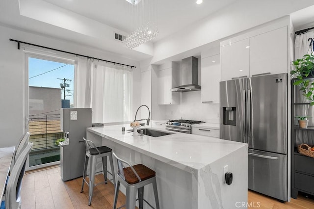 kitchen featuring white cabinets, sink, wall chimney exhaust hood, light wood-type flooring, and appliances with stainless steel finishes