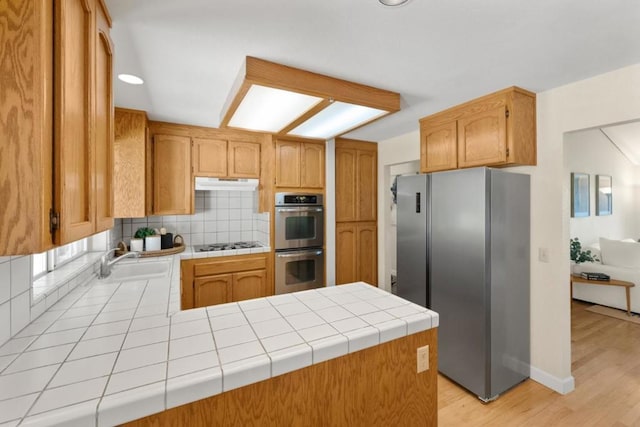 kitchen featuring kitchen peninsula, tasteful backsplash, appliances with stainless steel finishes, tile countertops, and light hardwood / wood-style floors