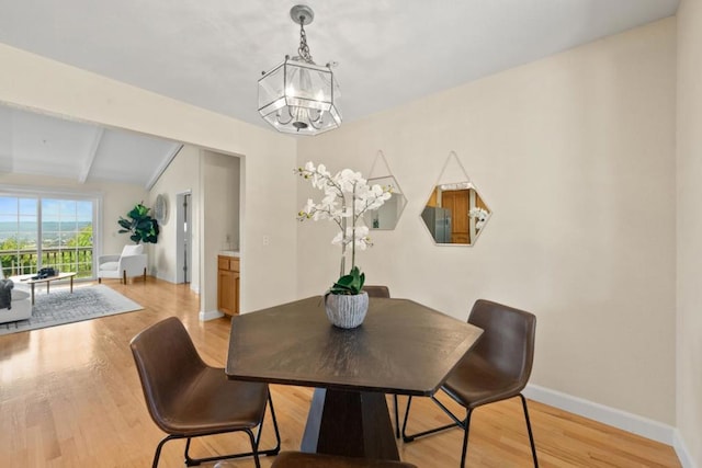 dining space featuring vaulted ceiling with beams, a notable chandelier, and light hardwood / wood-style flooring