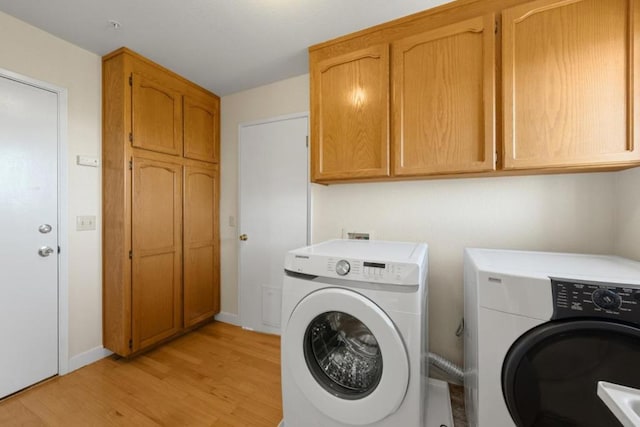 laundry room with washing machine and clothes dryer, light hardwood / wood-style flooring, and cabinets