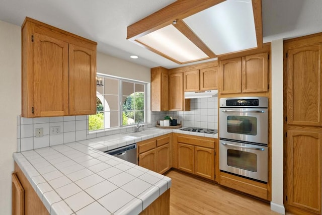 kitchen featuring light wood-type flooring, tile counters, sink, decorative backsplash, and stainless steel appliances