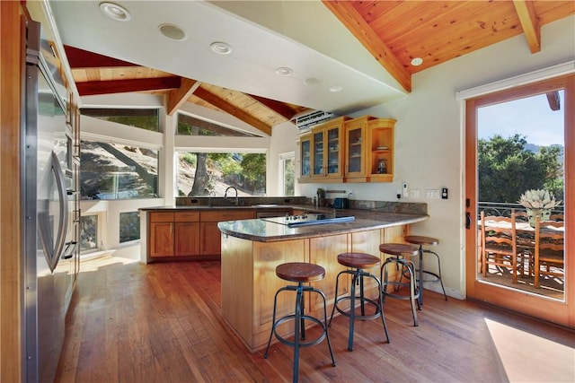 kitchen with kitchen peninsula, high quality fridge, hardwood / wood-style flooring, vaulted ceiling with beams, and a breakfast bar area