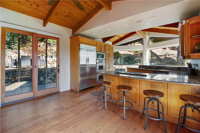 kitchen with built in appliances, vaulted ceiling with beams, a kitchen bar, and kitchen peninsula