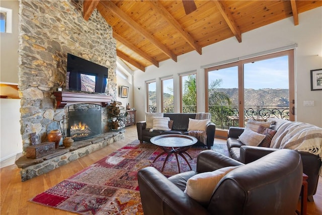 living room with wooden ceiling, high vaulted ceiling, a stone fireplace, hardwood / wood-style flooring, and beam ceiling