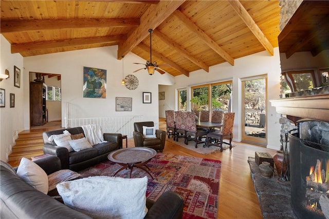 living room with wood ceiling, ceiling fan, beamed ceiling, light hardwood / wood-style floors, and a stone fireplace