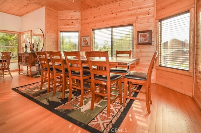 dining space with light hardwood / wood-style floors, wooden ceiling, and wooden walls