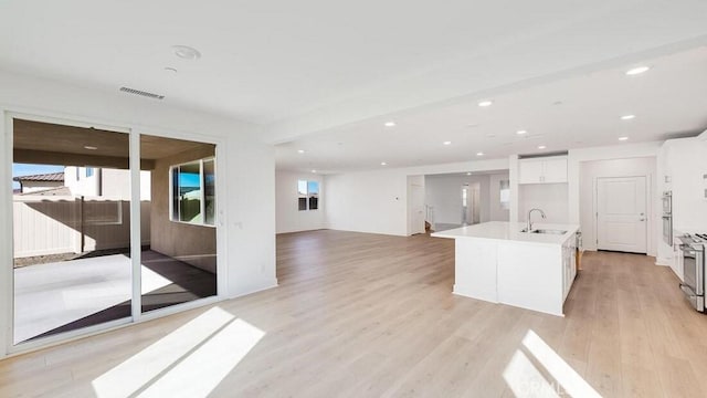 kitchen featuring sink, a center island with sink, light hardwood / wood-style flooring, stainless steel stove, and white cabinetry