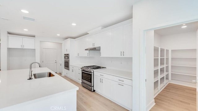 kitchen with gas stove, light hardwood / wood-style flooring, white cabinetry, and sink