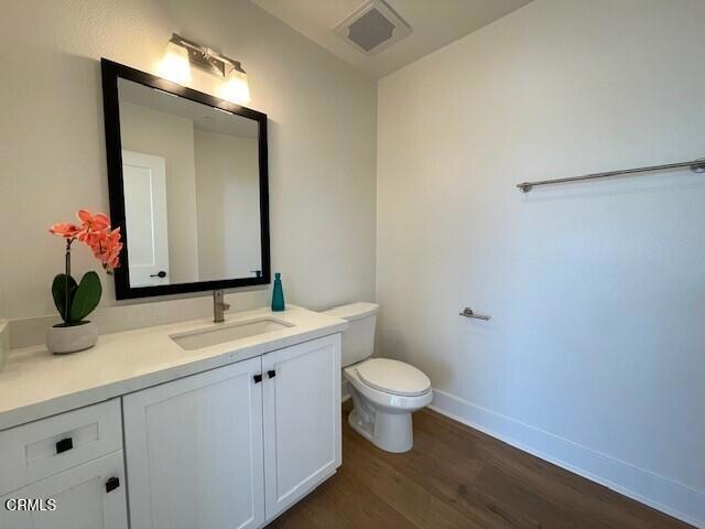 bathroom with visible vents, toilet, vanity, wood finished floors, and baseboards