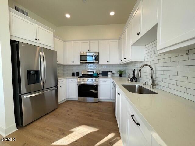 kitchen featuring stainless steel appliances, backsplash, white cabinets, a sink, and light wood-type flooring