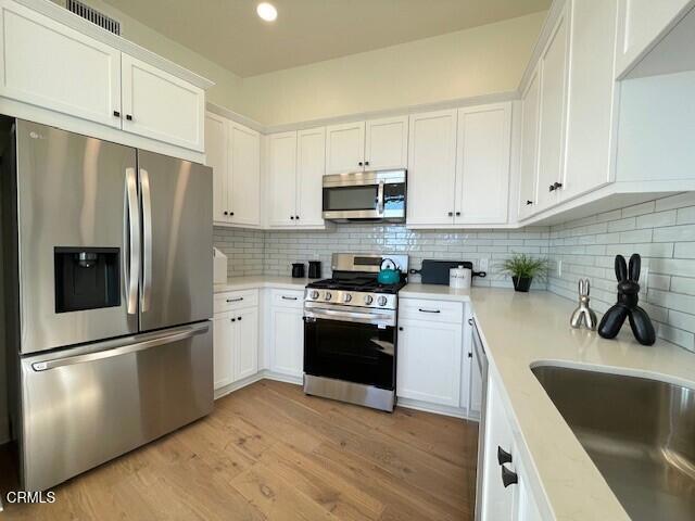 kitchen with white cabinets, a sink, stainless steel appliances, light countertops, and backsplash