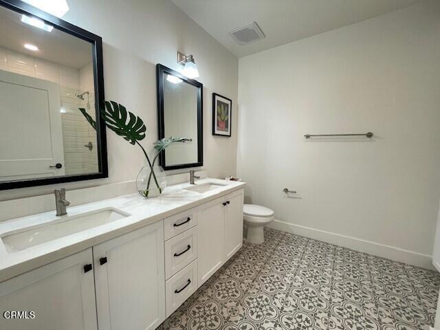 bathroom with toilet, a sink, baseboards, and double vanity