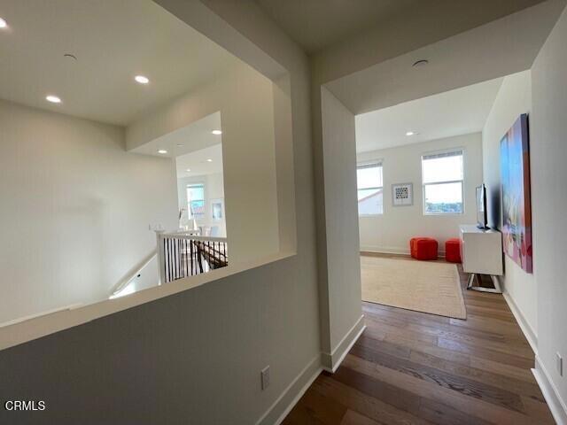 hallway featuring recessed lighting, baseboards, wood finished floors, and an upstairs landing