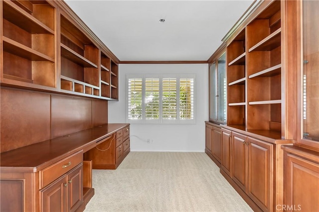 unfurnished office featuring crown molding, light colored carpet, and built in desk