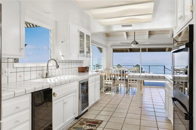 kitchen with a water view, wine cooler, tile counters, and tasteful backsplash