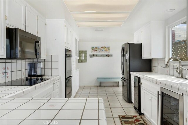 kitchen featuring white cabinets, wine cooler, backsplash, black appliances, and tile counters