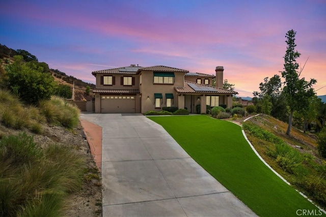 mediterranean / spanish house featuring a garage, a yard, and solar panels