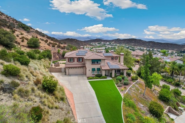 view of front of house with solar panels, a garage, a front lawn, and a mountain view