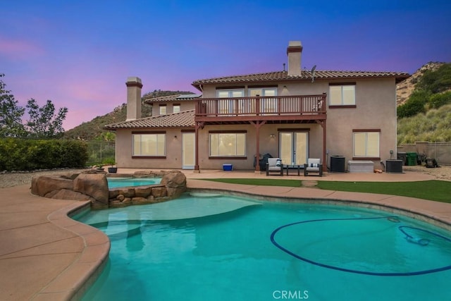 back house at dusk featuring a pool with hot tub, central AC, french doors, and a patio