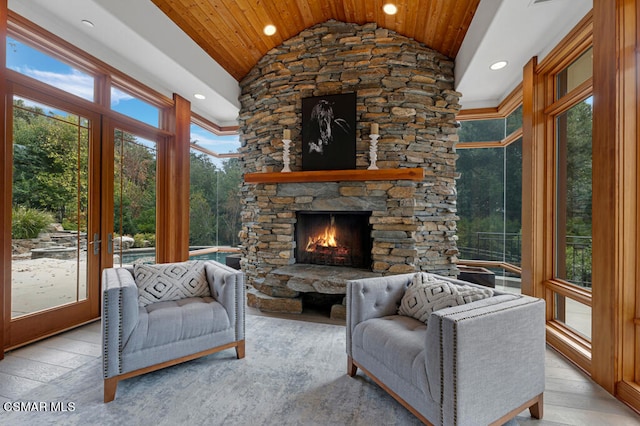 living room featuring vaulted ceiling, a stone fireplace, light hardwood / wood-style floors, and wood ceiling