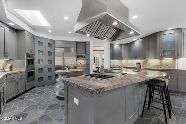 kitchen with a kitchen breakfast bar, a skylight, built in appliances, and island range hood