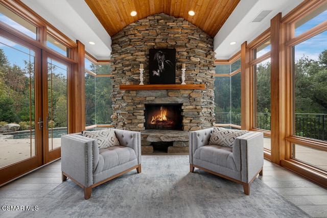 sunroom / solarium with wood ceiling, vaulted ceiling, a stone fireplace, and plenty of natural light