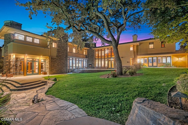 back house at dusk with french doors, a patio, and a yard