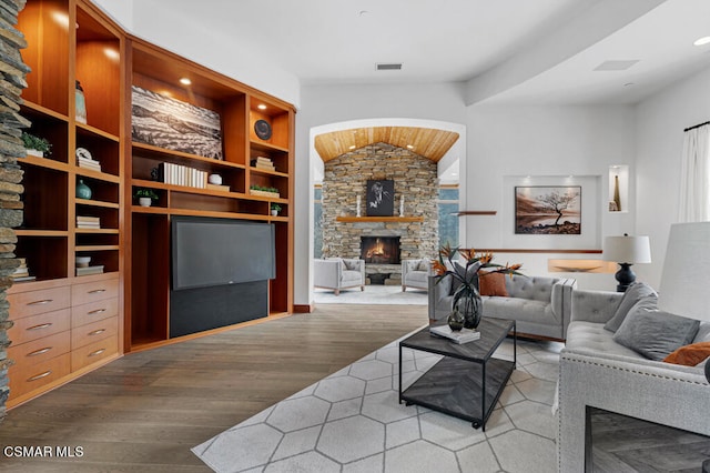 living room featuring built in shelves, hardwood / wood-style floors, vaulted ceiling, and a fireplace