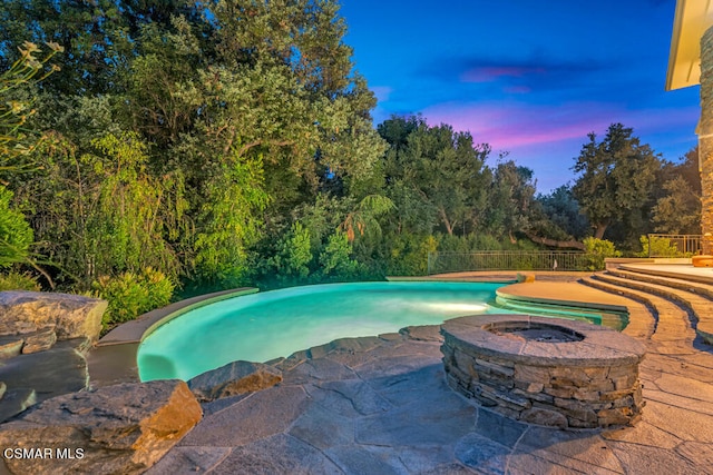 pool at dusk featuring an in ground hot tub and a patio