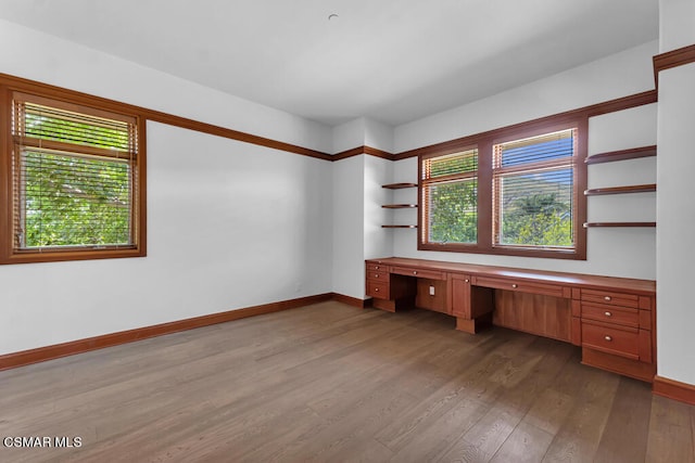 unfurnished office with built in desk, a healthy amount of sunlight, and dark wood-type flooring