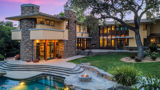 back house at dusk featuring a patio, a yard, and a balcony