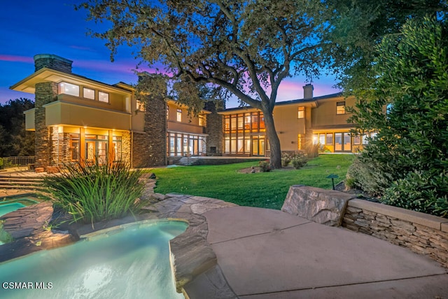 back house at dusk with a patio area and a lawn