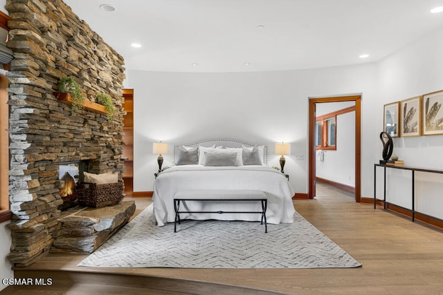 bedroom with a stone fireplace and light hardwood / wood-style floors