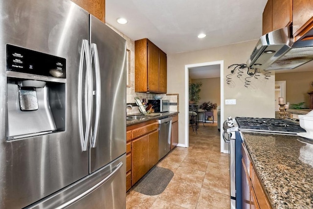 kitchen with appliances with stainless steel finishes, tasteful backsplash, ventilation hood, light tile patterned flooring, and dark stone counters