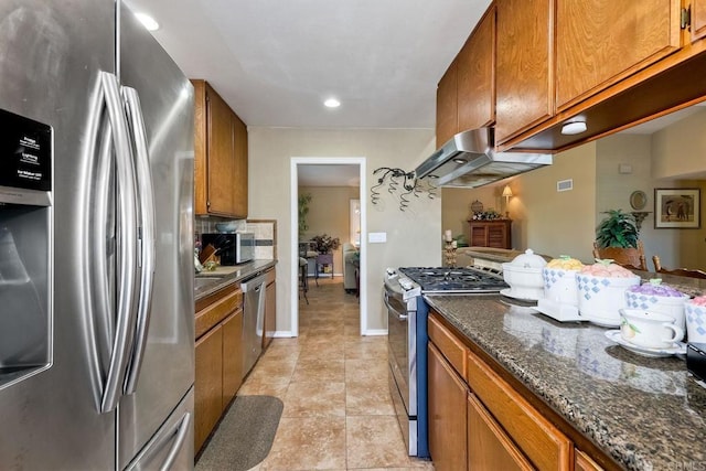 kitchen with ventilation hood, light tile patterned floors, appliances with stainless steel finishes, dark stone counters, and decorative backsplash