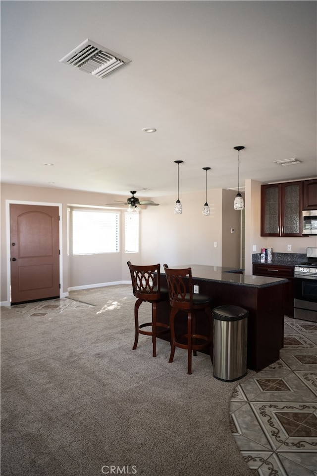 kitchen featuring appliances with stainless steel finishes, a kitchen bar, carpet flooring, dark brown cabinets, and ceiling fan