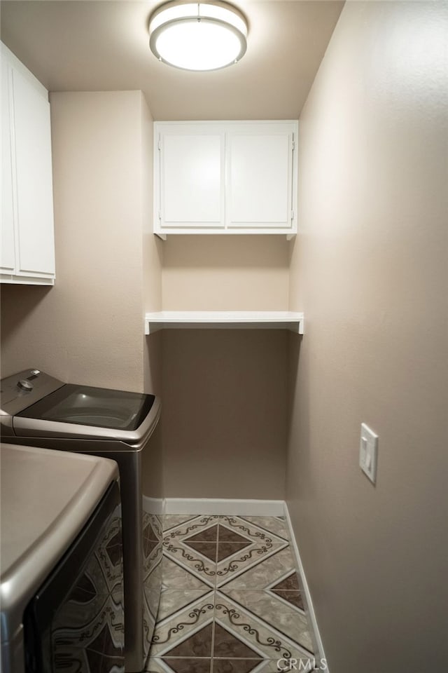 clothes washing area with cabinets, tile patterned flooring, and washing machine and clothes dryer