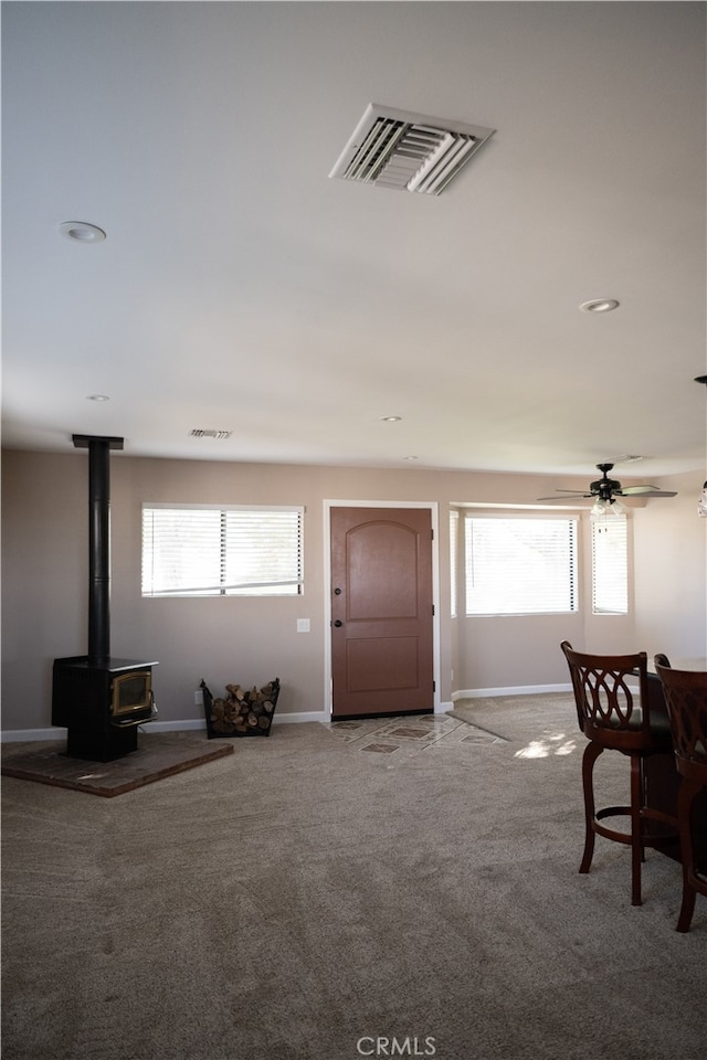 entryway with ceiling fan, carpet flooring, and a wood stove