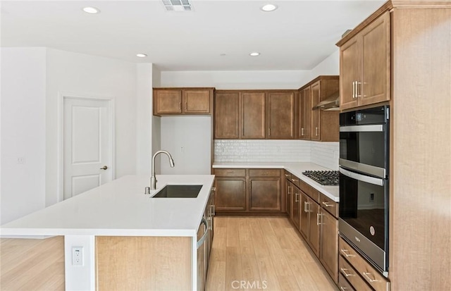 kitchen featuring tasteful backsplash, visible vents, light countertops, light wood-type flooring, and a sink