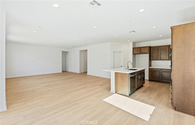 kitchen featuring light wood-style flooring, a sink, visible vents, tasteful backsplash, and an island with sink