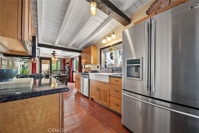 kitchen featuring ceiling fan, stainless steel appliances, vaulted ceiling with beams, dark stone counters, and dark tile patterned floors