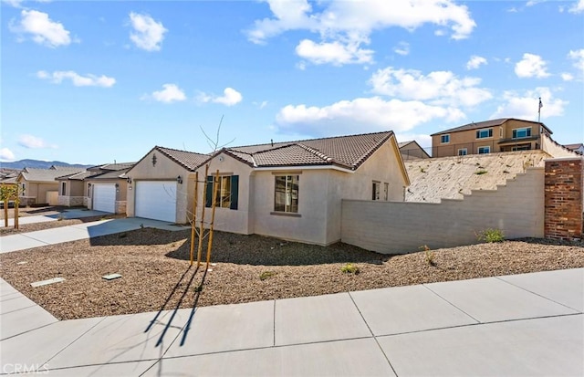 view of front facade featuring an attached garage, fence, a tiled roof, driveway, and stucco siding