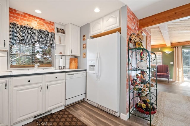 kitchen with dark hardwood / wood-style flooring, white cabinets, brick wall, white appliances, and beamed ceiling