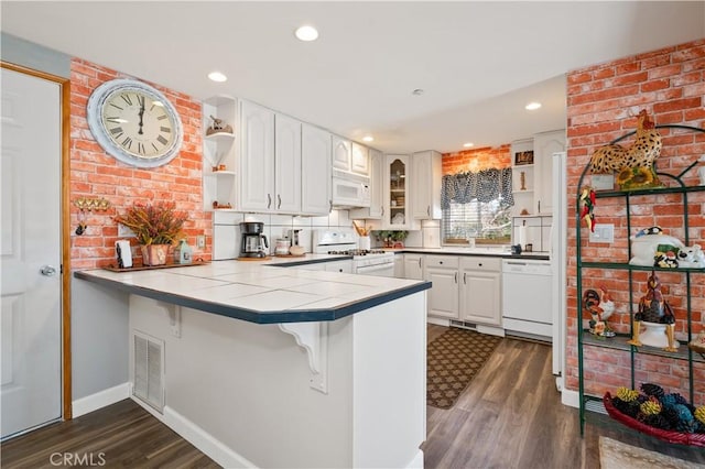 kitchen featuring dark wood-type flooring, kitchen peninsula, tile countertops, white appliances, and white cabinets