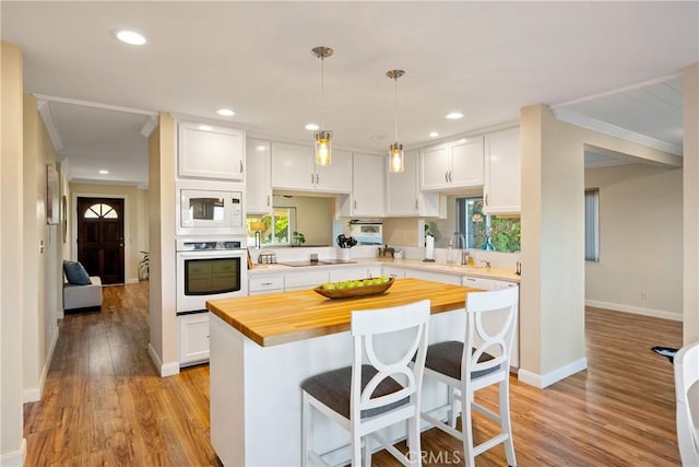 kitchen featuring white appliances, a kitchen breakfast bar, white cabinetry, and butcher block countertops